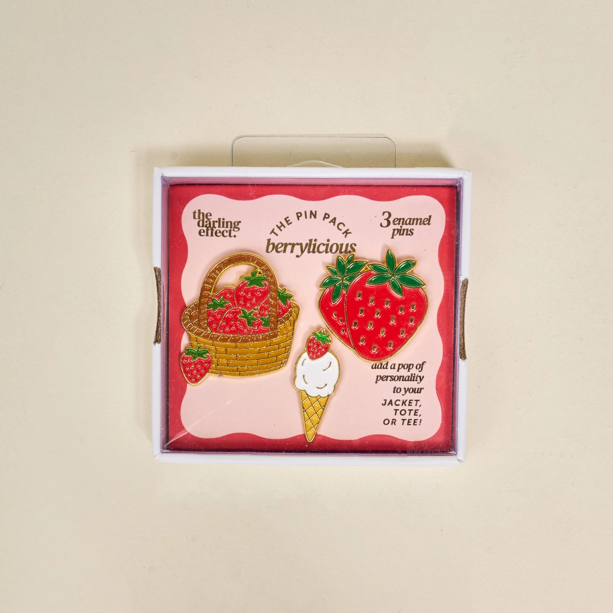 Set of berry-themed enamel pins in a decorative box on a beige background