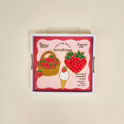 Set of berry-themed enamel pins in a decorative box on a beige background