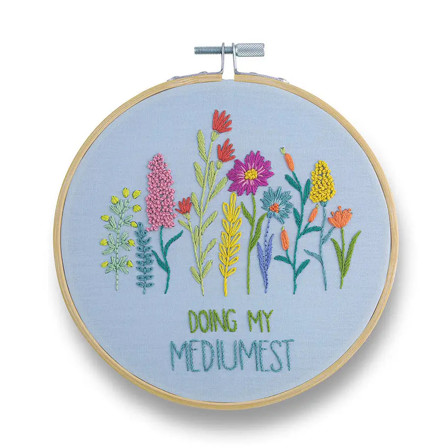 Embroidery hoop with floral design and text 'Doing My Mediumest' on a light blue background