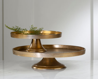 Two round, gold-colored pedestals on a white background with a sprig of greenery on top of one