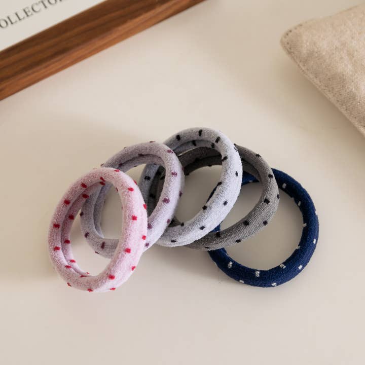 5 polka dot hair ties in pink, blue, and assorted grey hues arranged on a taupe background