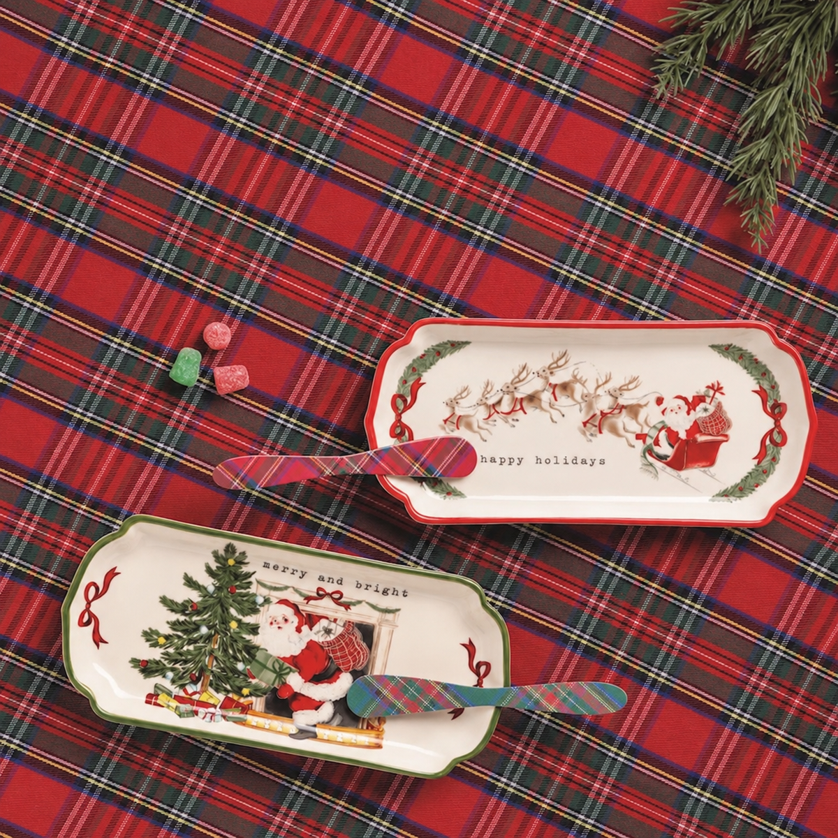 Two Christmas-themed rectangular serving trays displayed on a red tartan plaid fabric background. One tray features Santa Claus and a Christmas tree with the text 'happy and bright', and the other features Santa and reindeer with 'happy holidays'.