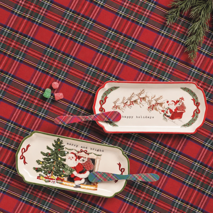 Two Christmas-themed rectangular serving trays displayed on a red tartan plaid fabric background. One tray features Santa Claus and a Christmas tree with the text 'happy and bright', and the other features Santa and reindeer with 'happy holidays'.