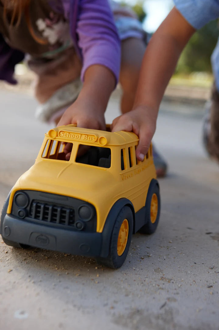 childern's hands pushing school bus down a sidewalk.