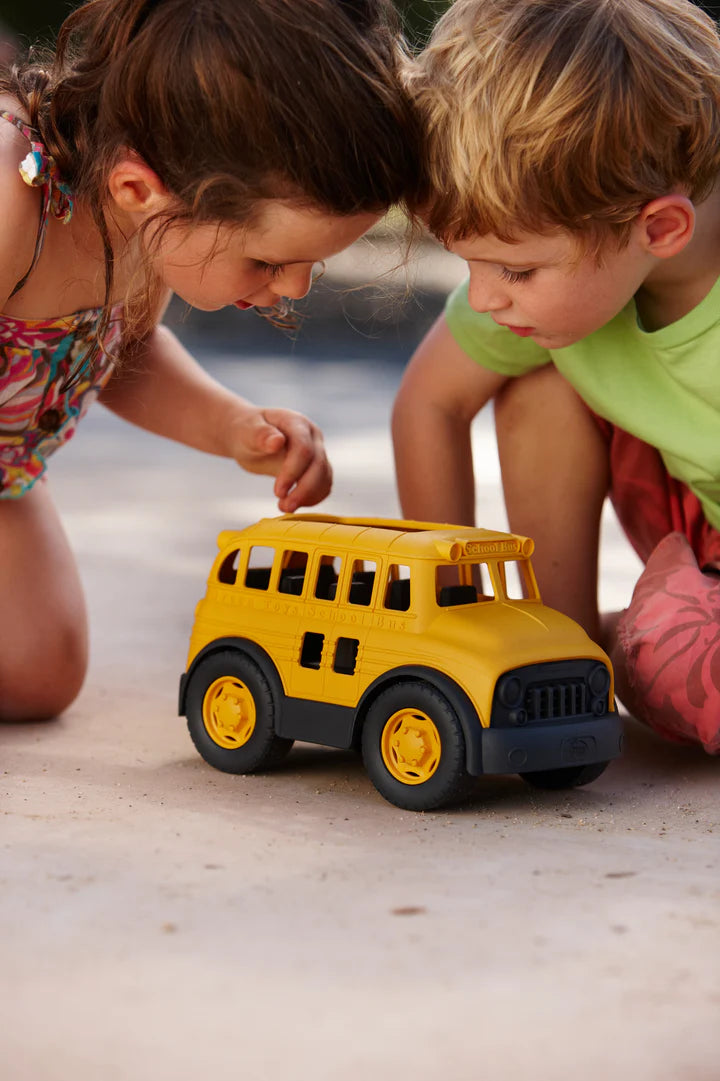 2 small children playing with school bus outside.