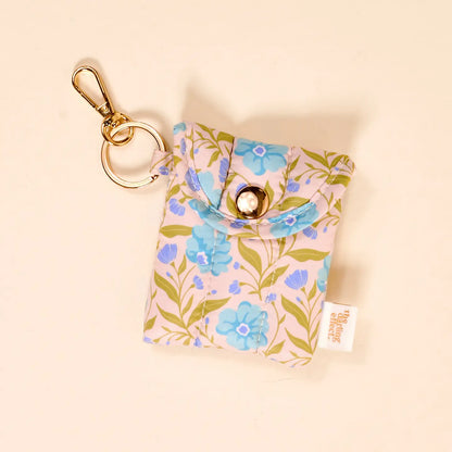 Floral patterned ear bud pouch with keychain on a beige background