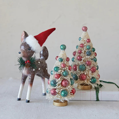 fawn wearing a red hat set next to 2 decorative trees.