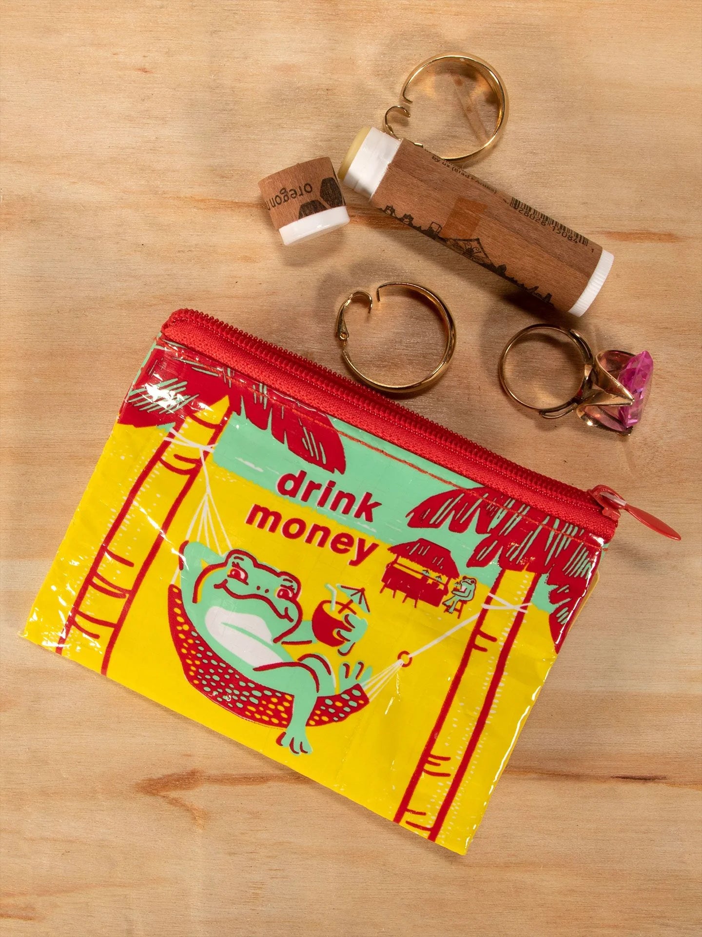 drink money coin purse laying on a wooden table next to chap stick and jewelry.