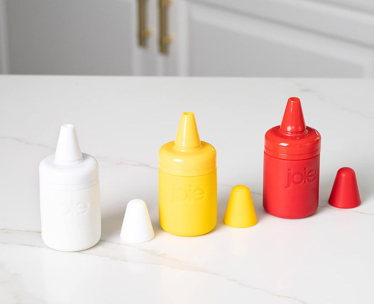Set of 3 condiment bottles each with their loids set next to them on a white surface.
