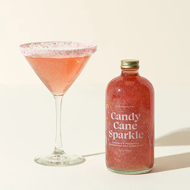 Bottle of 'Candy Cane Sparkle' cocktail mix next to a cocktail glass filled with the drink on a light background.