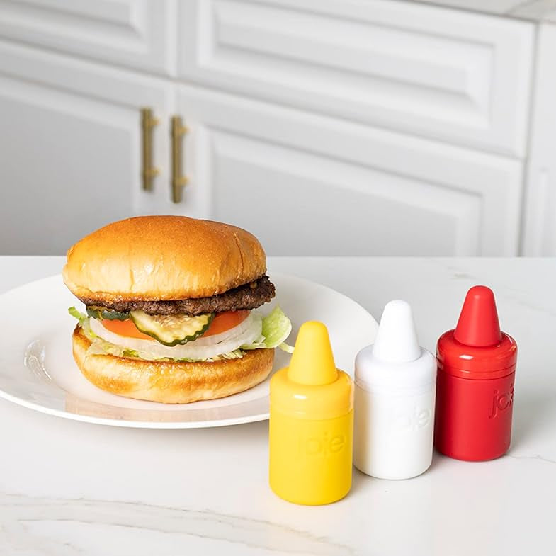 Hamburger on a plate with mini condiment bottles set next to it on a kitchen counter
