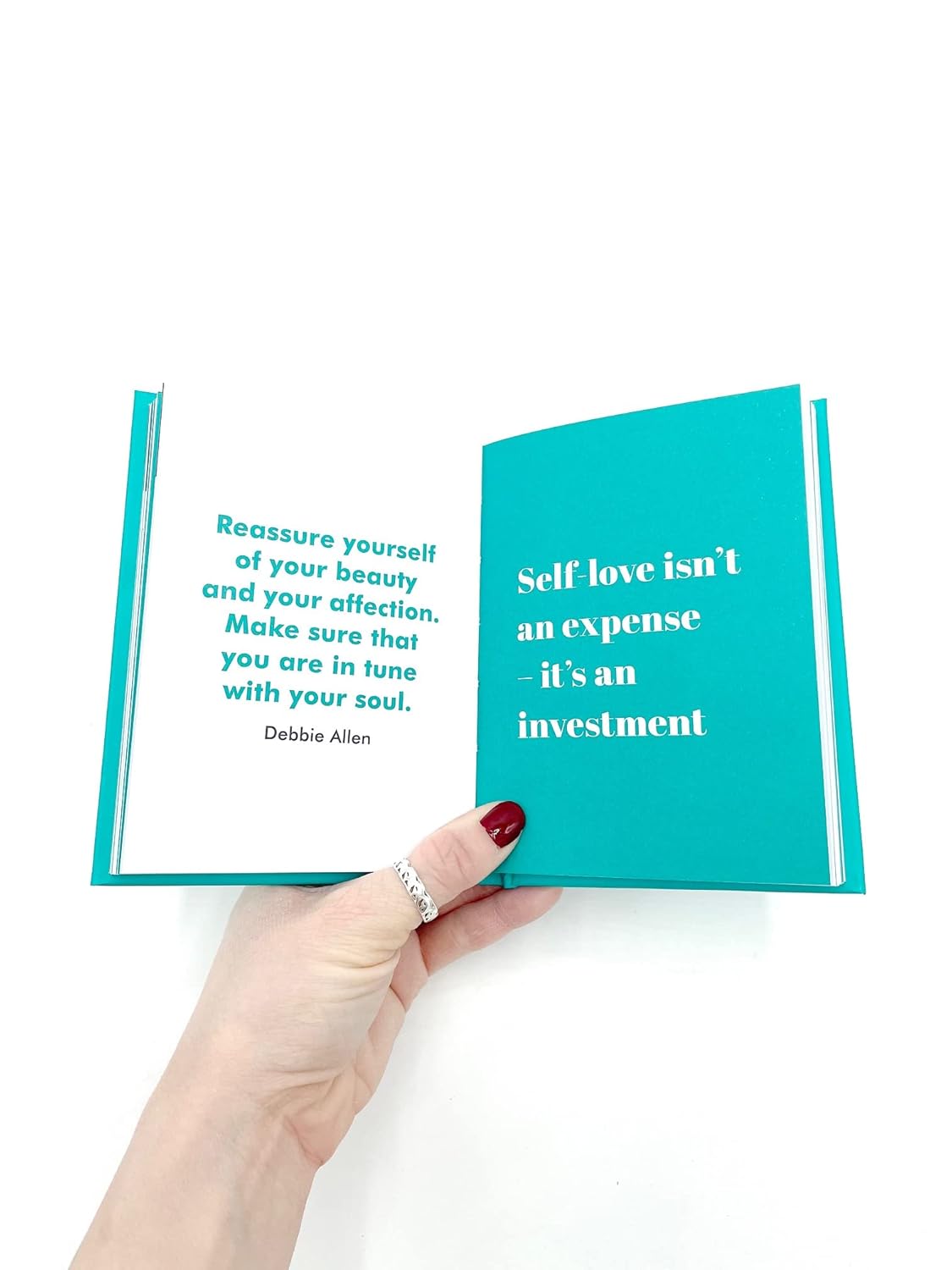Hand holding a teal book with motivational quote on a white background
