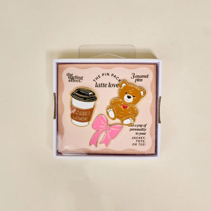 Set of three enamel pins in a box with a teddy bear, coffee cup, and pink bow design.