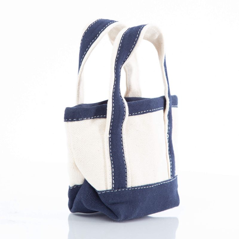 angled view of off white mini tote bag with navy blue handles and trim