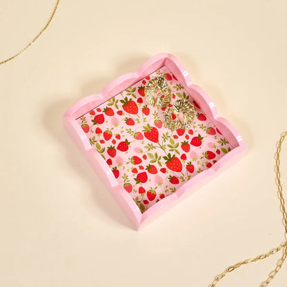 small tray with strawberry pattern with gold earrings in it shown on a beige background