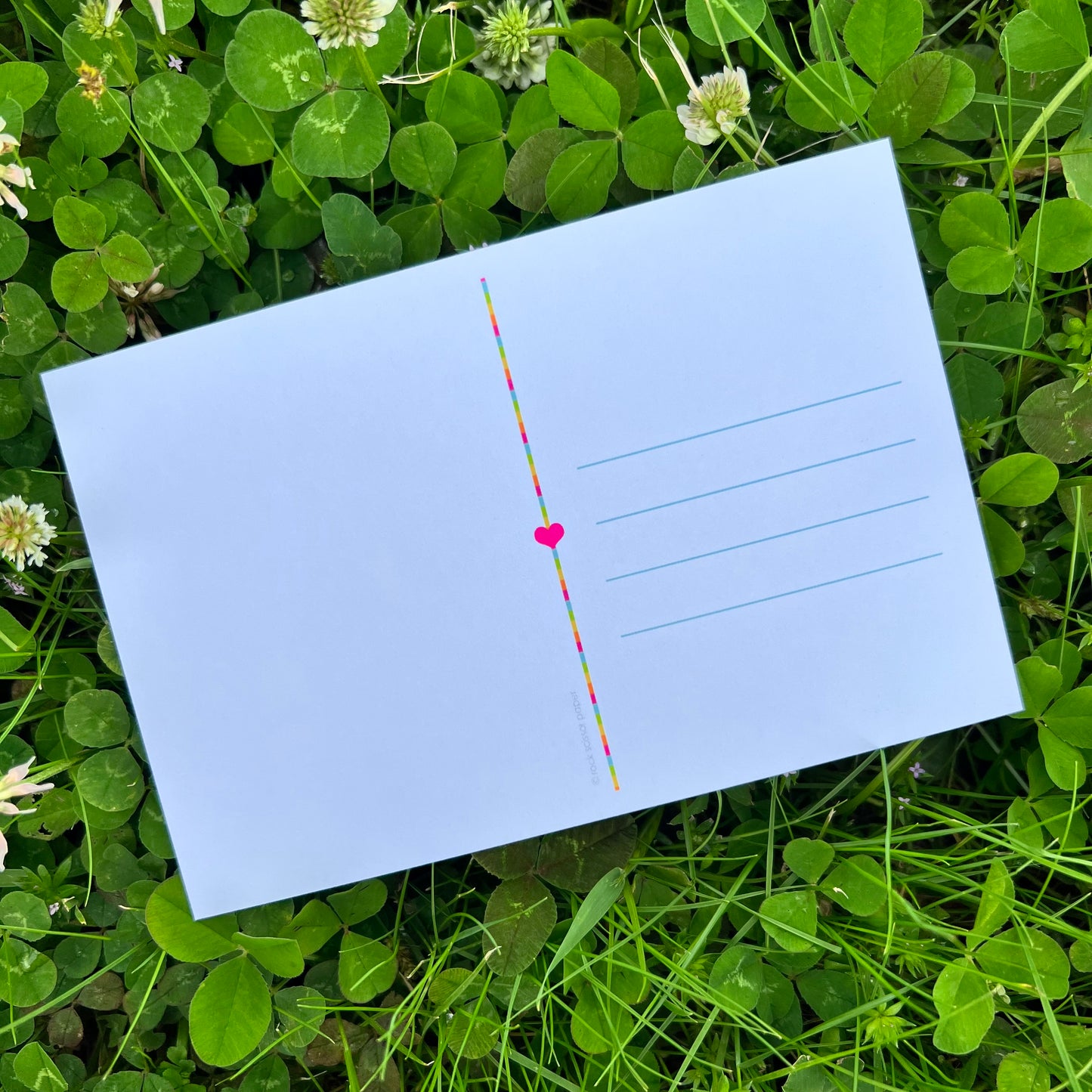 back of post card with address lines and pink heart laying in a field of clovers.