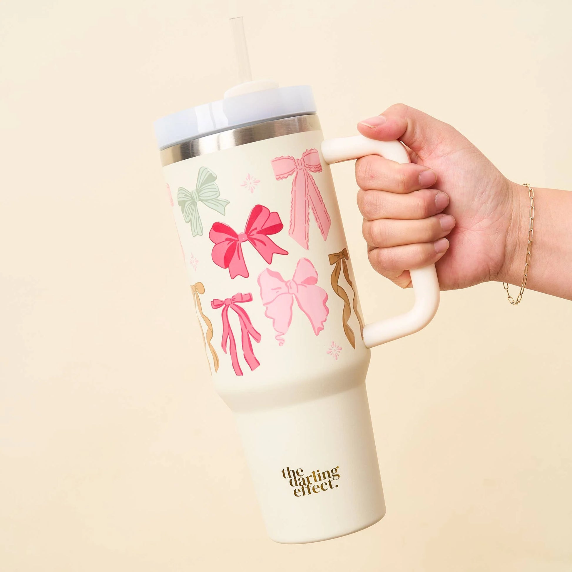 hand holding bow affair tumbler that is off-white with pink and green bows printed on it.