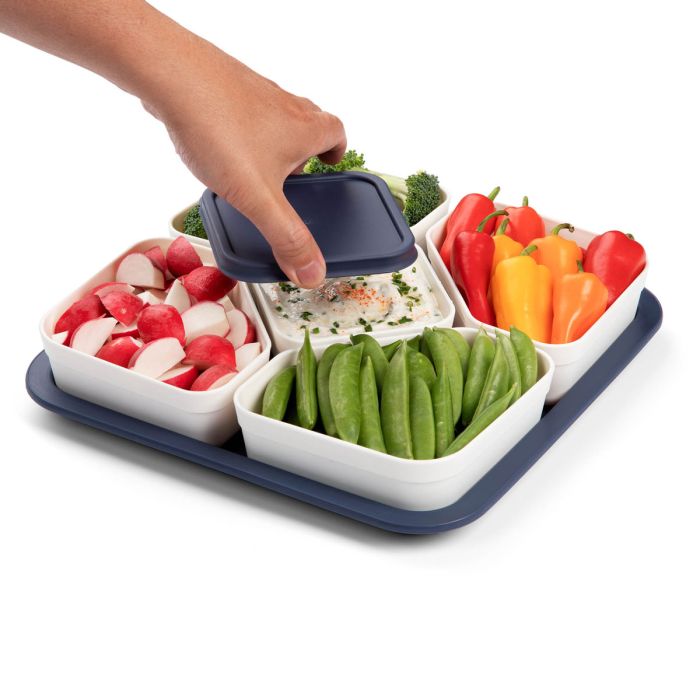 Party Carrier filled with veggies in corner bowls and dip in the center with a hand removing the lid
