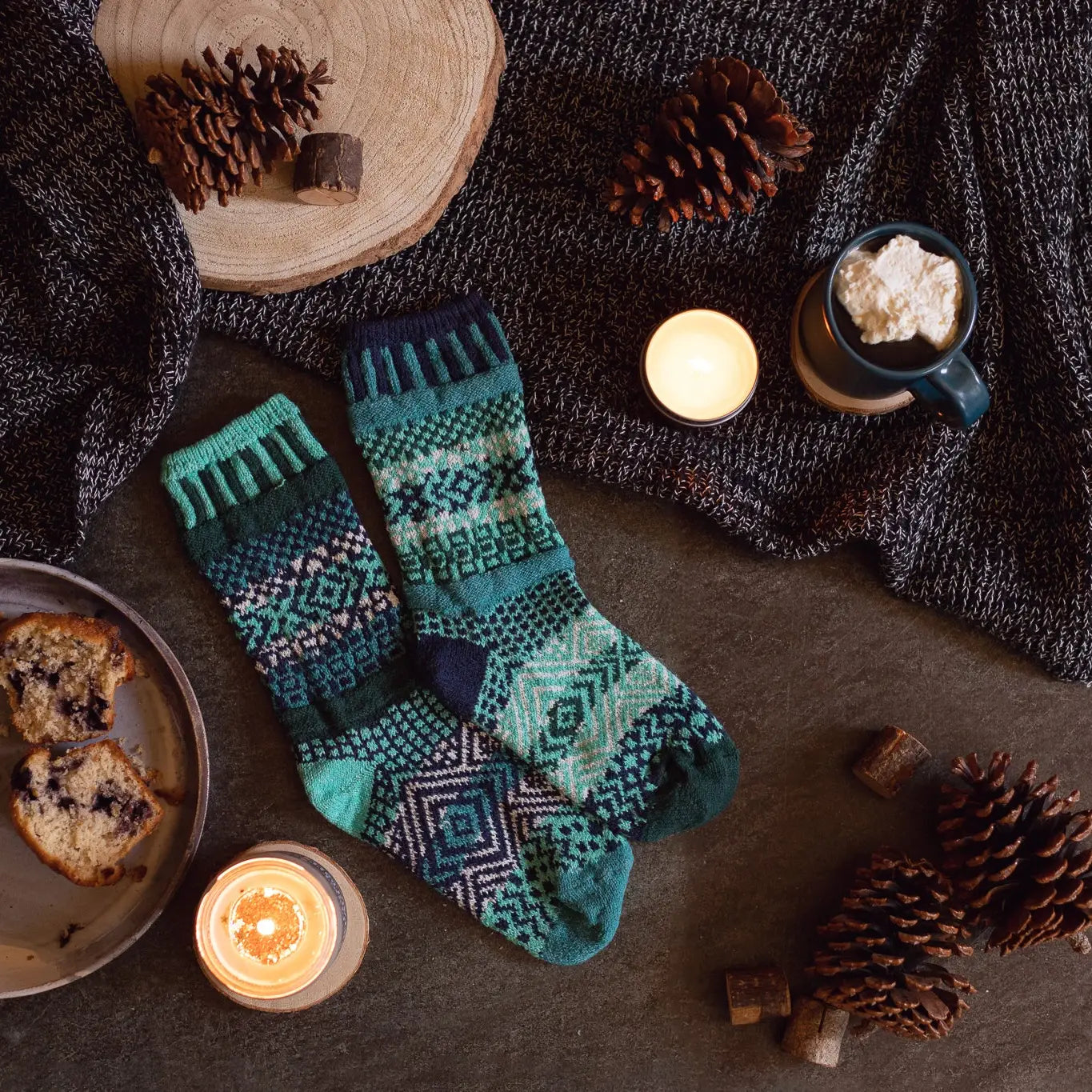 pair of Evergreen Crew Socks on the floor surrounded by cocoa, muffins, and pinecones