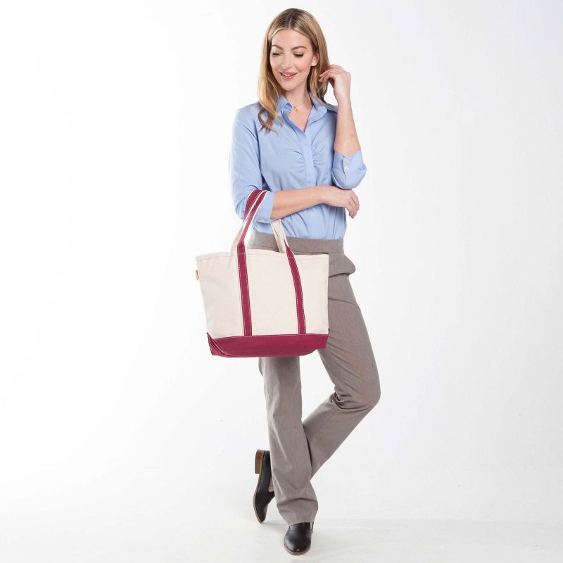 a person wearing grey slacks and light blue top holding off white tote with maroon trim and handles