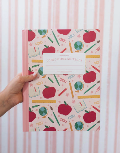 Composition notebook with apple and school supplies pattern held by a hand against a striped background