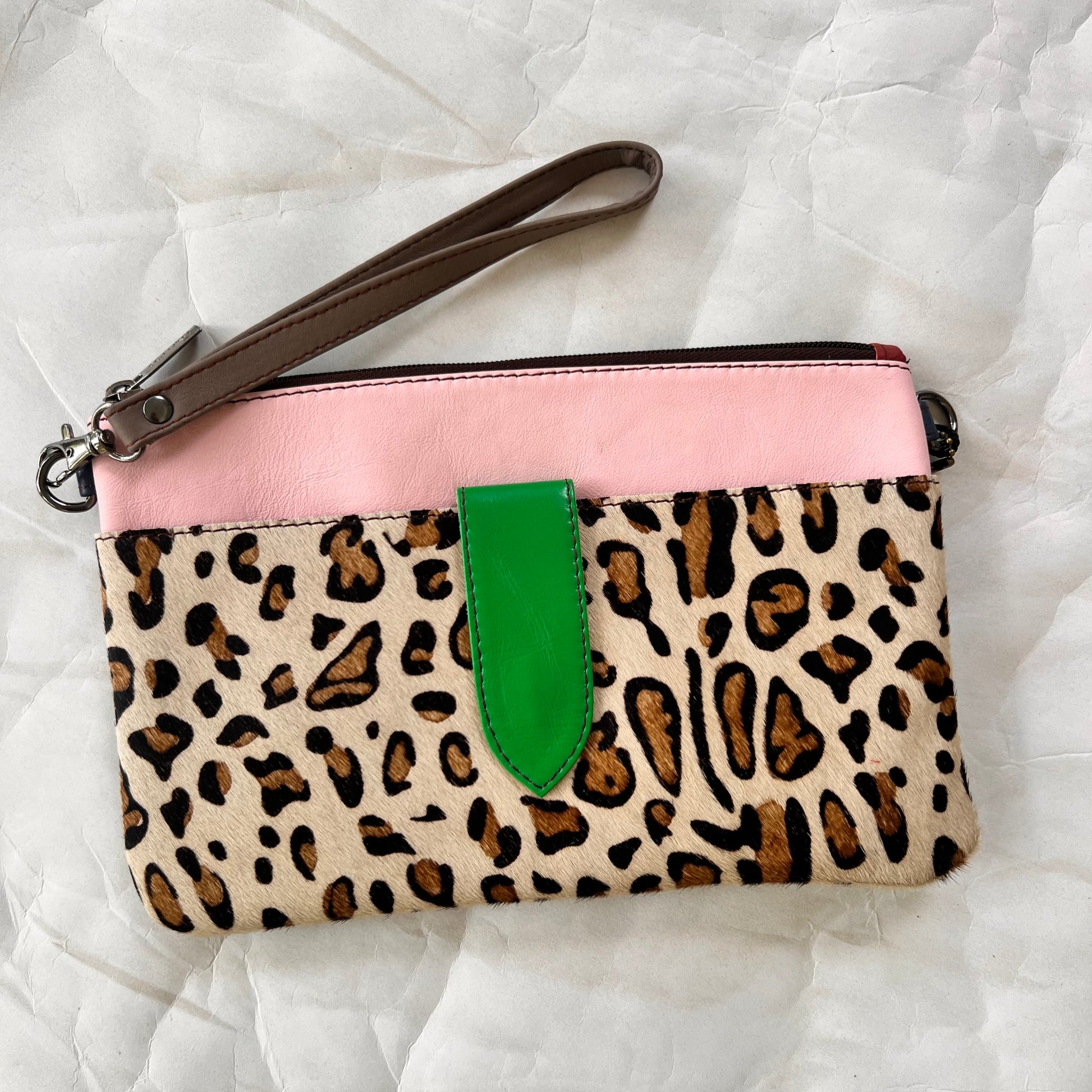 green rectangular bag with cheetah print pocket, green tab, and grey wristlet strap.