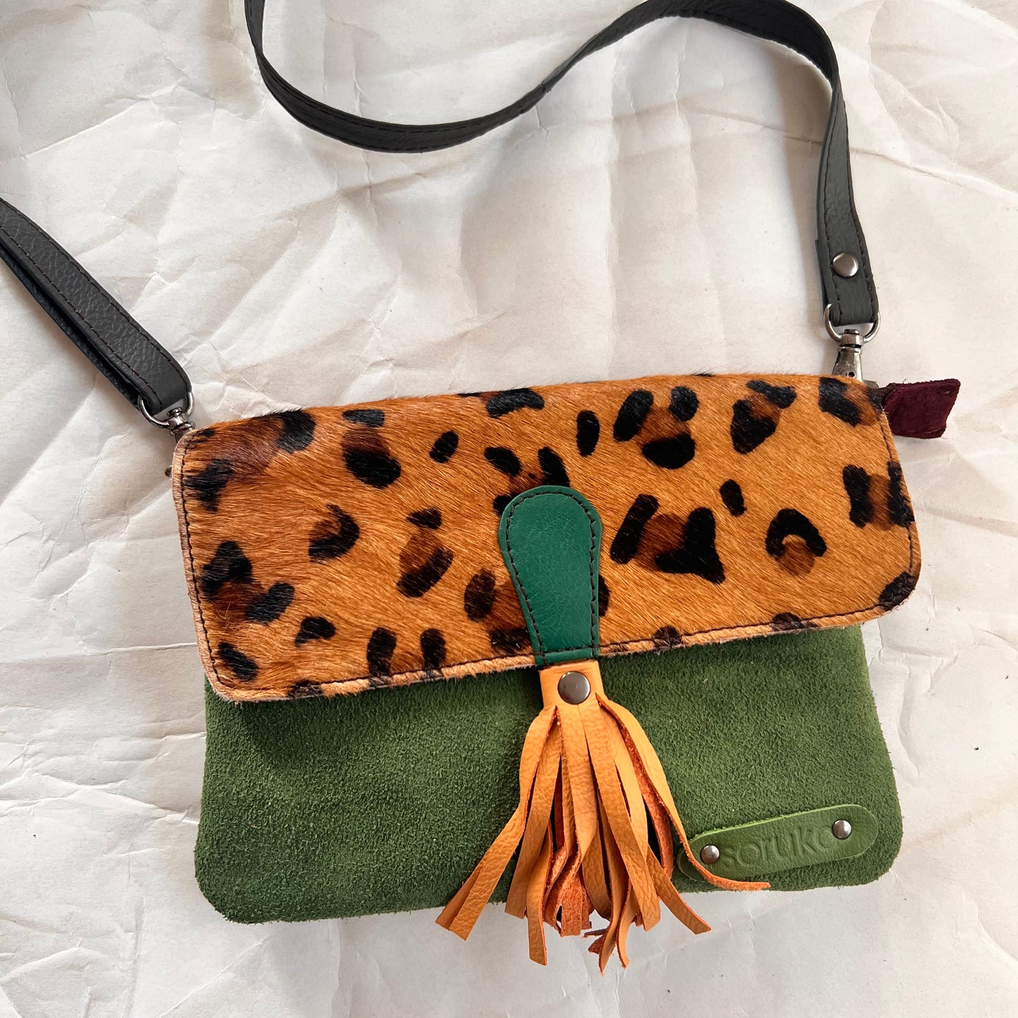 juliette bag with animal print flap, peach tassel, and crossbody strap clipped on it.