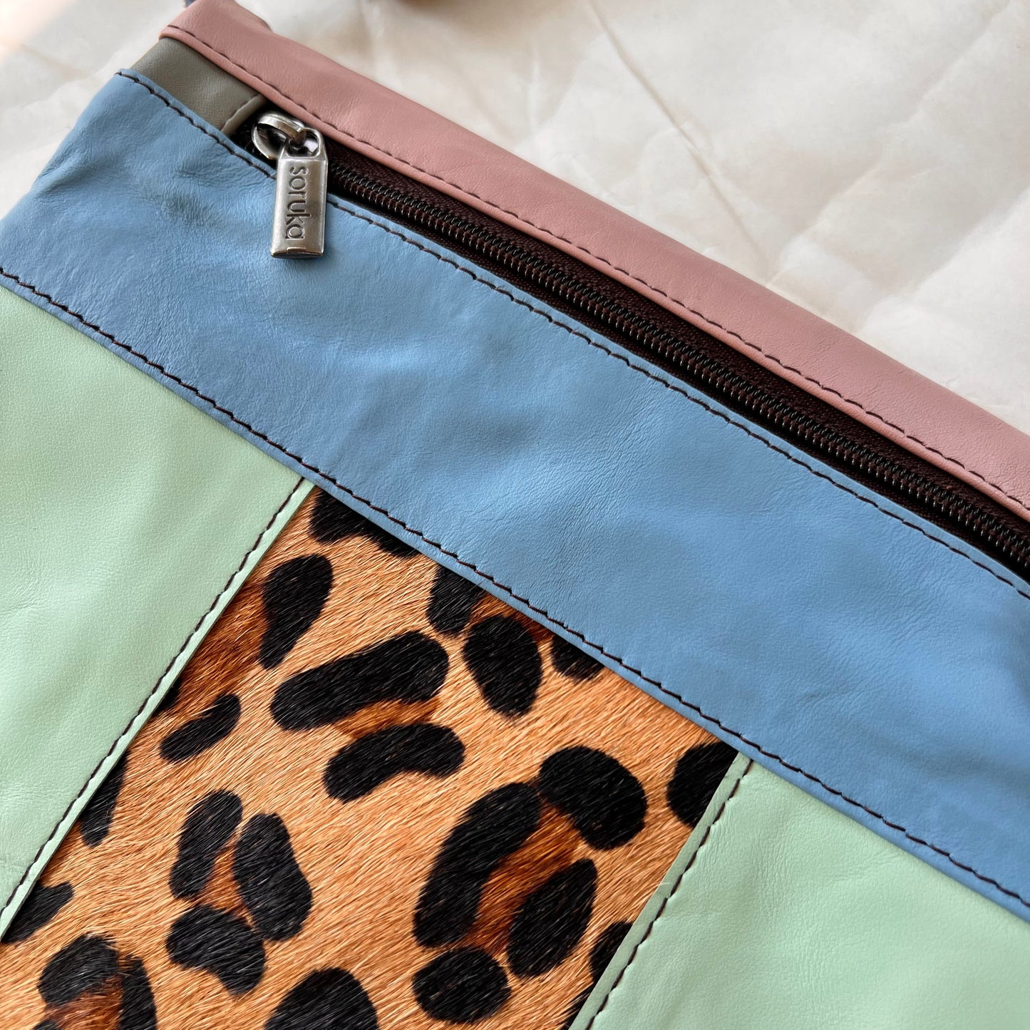 close-up of seafoam greta bag with animal print block in the center with blue stripe and zipper across the top.