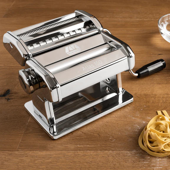 Atlas Classic Pasta Machine set on a wooden surface with a pile of fresh pasta next to it