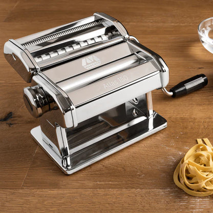 Atlas Classic Pasta Machine set on a wooden surface with a pile of fresh pasta next to it