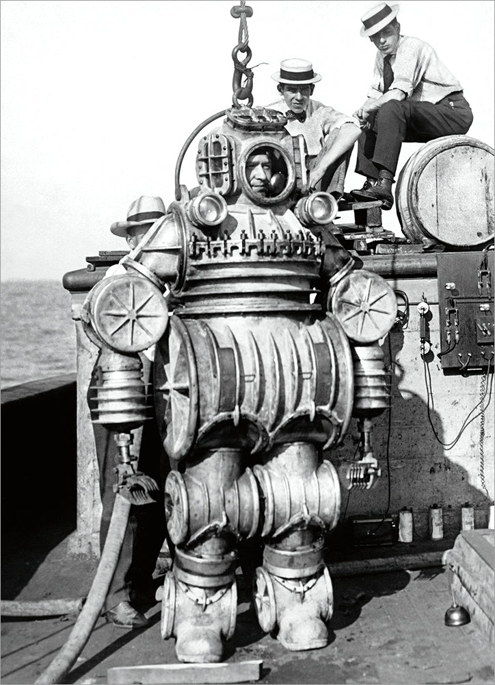 black and white image of person wearing old-fashion metal diving suit with others looking around.