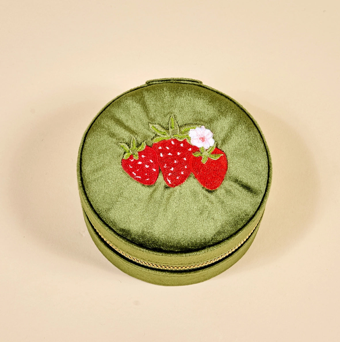 Round green jewelry case with strawberry design on a beige background