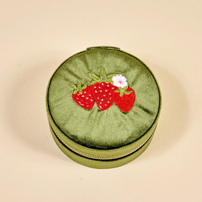 Round green jewelry case with strawberry design on a beige background