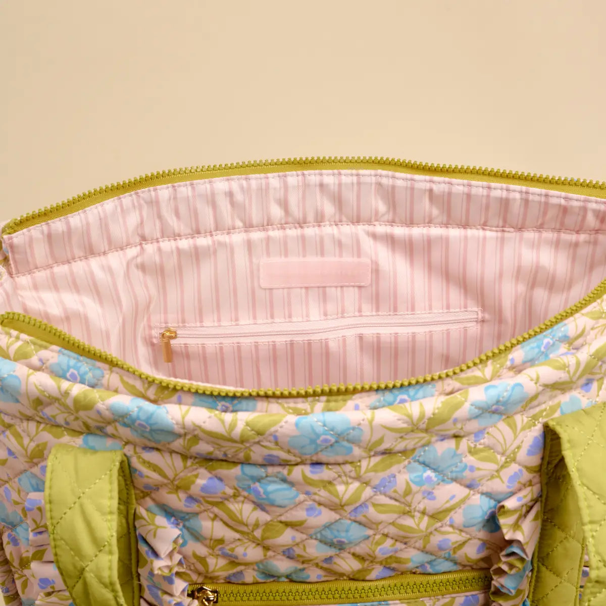 Floral-patterned bag unzipped showing a pink stripe interior on a beige background