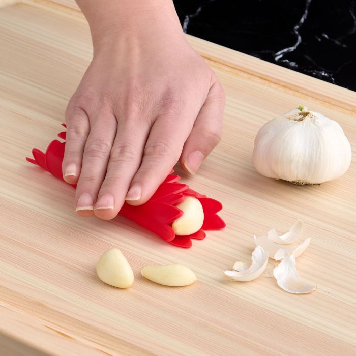 hand using red Silicone Jar Opener to peel garlic on a wooden surface