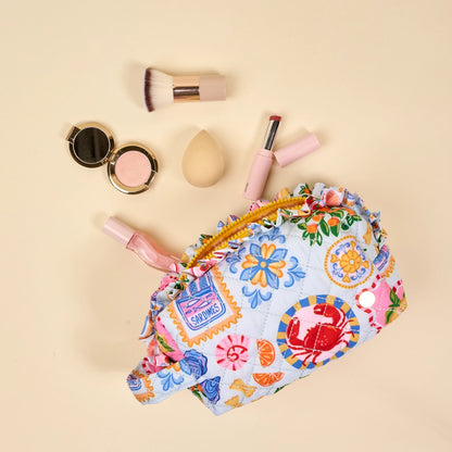 Colorful floral-patterned makeup bag with cosmetic items on a beige background