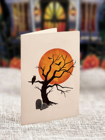 Halloween-themed card with a tree, moon, and owl on a textured surface.