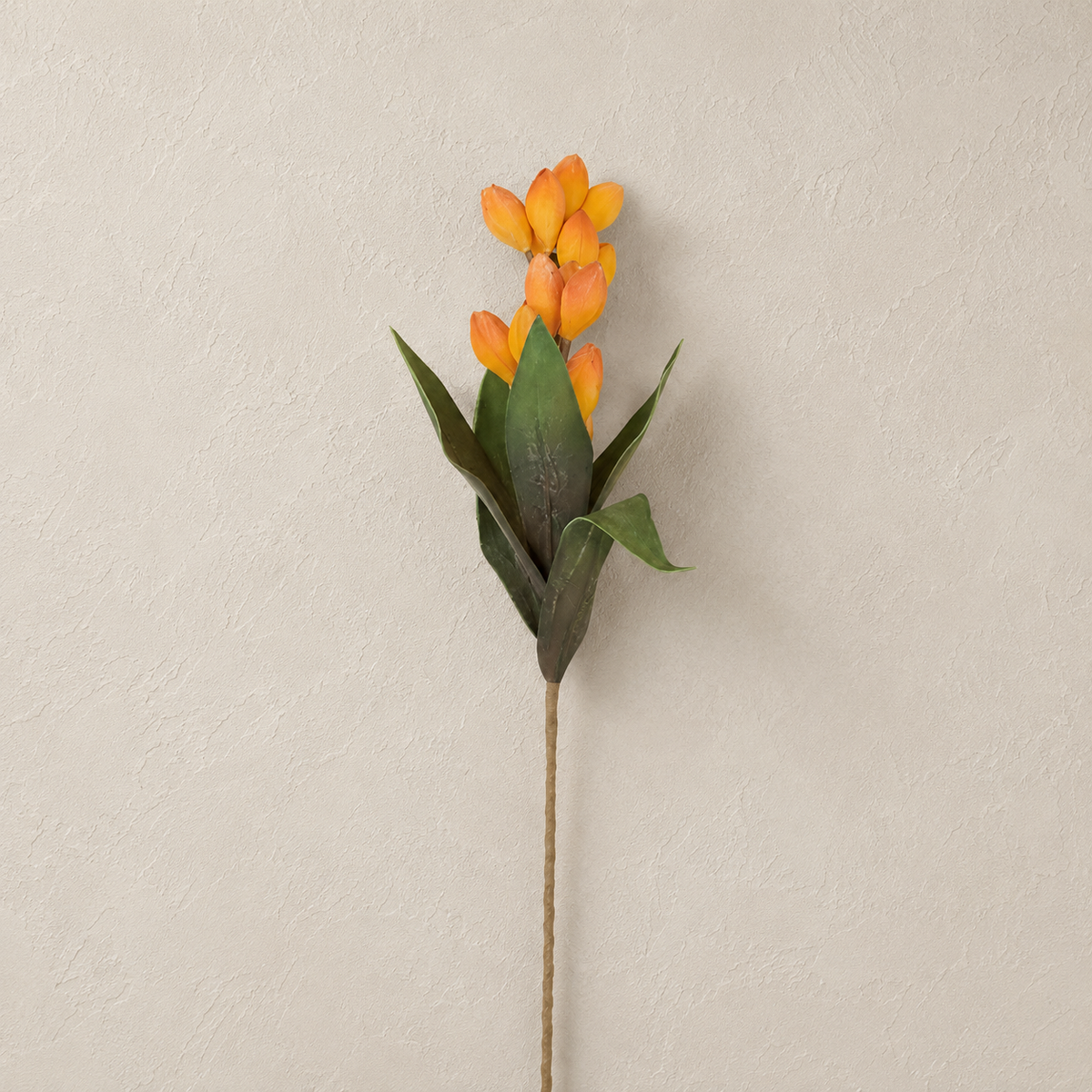 An artificial stem withyellow-orange pods and green leaves shown against a neutral, textured beige wall.