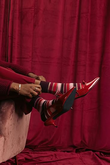 Person wearing red high heels and striped socks against a red curtain background