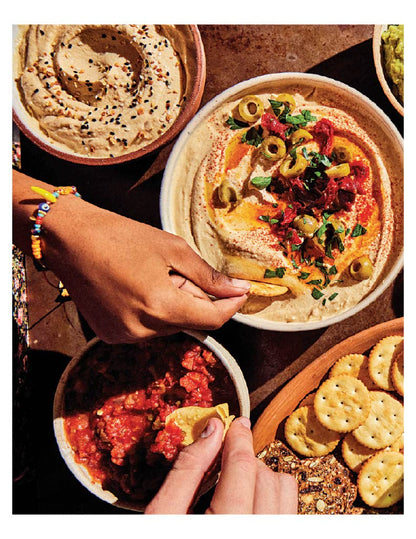 top view of a table with hands scooping assorted dips with crackers and chips.