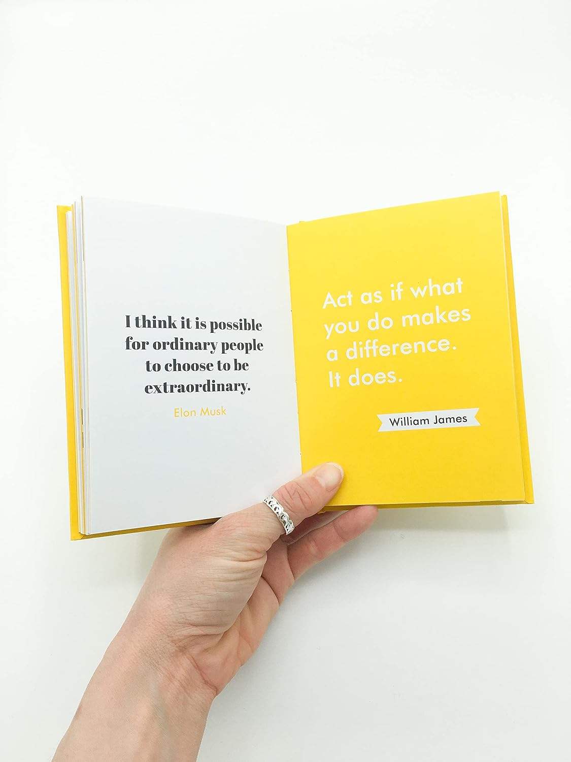 Hand holding an open book with a yellow cover and black text on a white background