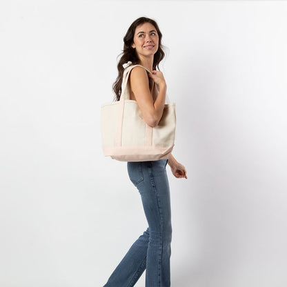a person wearing jeans and white top holding off white tote with pale pink trim and handles