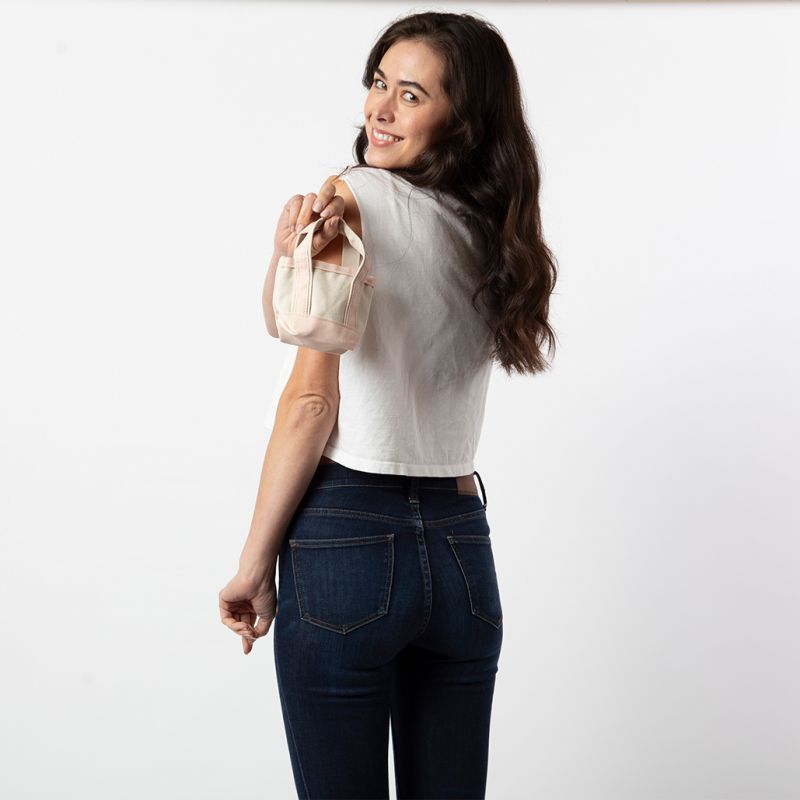 person wearing jeans and a white top holding off white mini tote bag with pale pink handles and trim