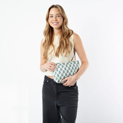 person wearing black jeans and a cream top holding a patterned clutch bag against a white background