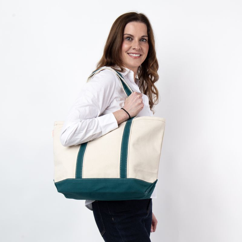 a person wearing black pants and white top holding off white tote with teal green trim and handles