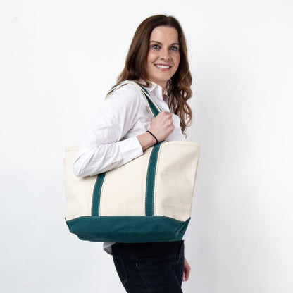 a person wearing black pants and white top holding off white tote with teal green trim and handles