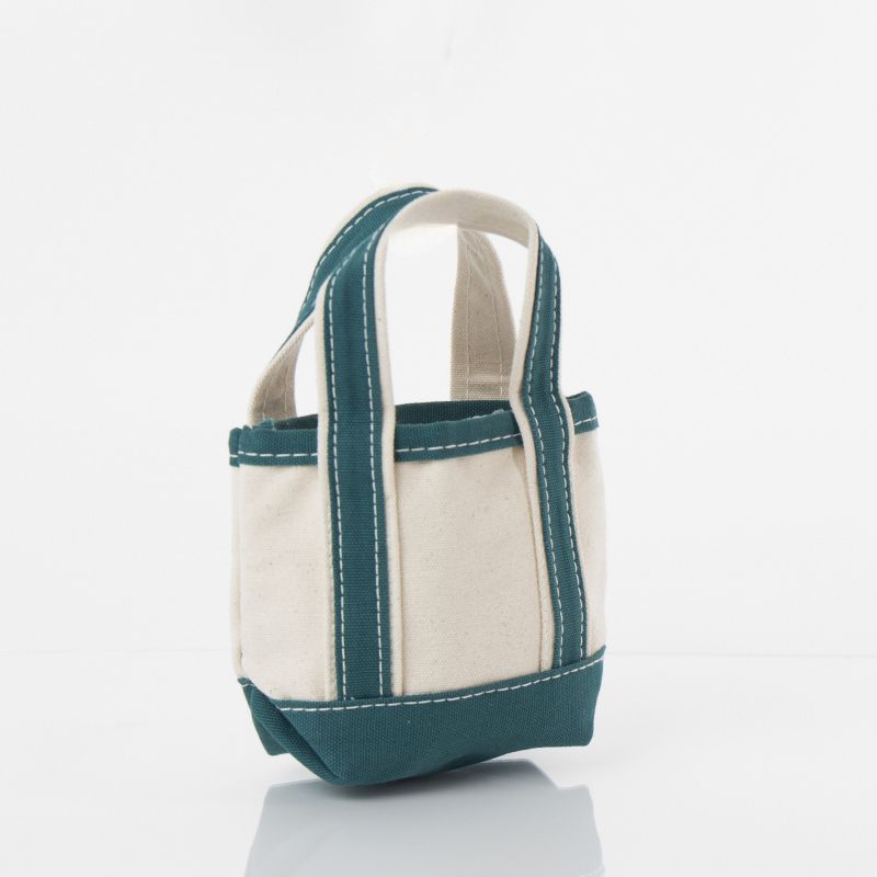 angled view of off white mini tote bag with teal green handles and trim