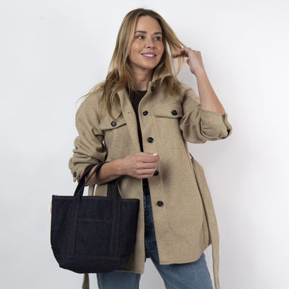 a person wearing jeans and khaki jacket holding the denim open tote  