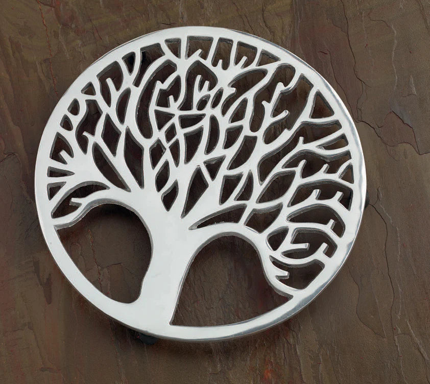 aluminum trivet with tree design set on a wooden table.