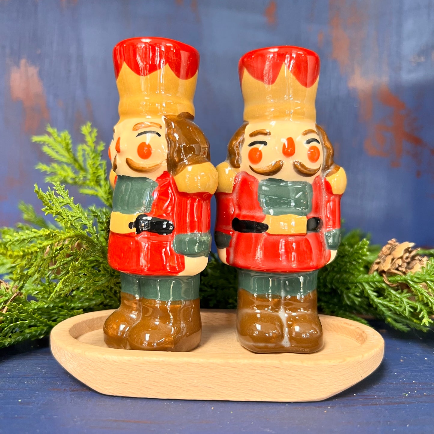 nutcracker salt and pepper shakers on a wooden tray in front of greenery and a blue background.